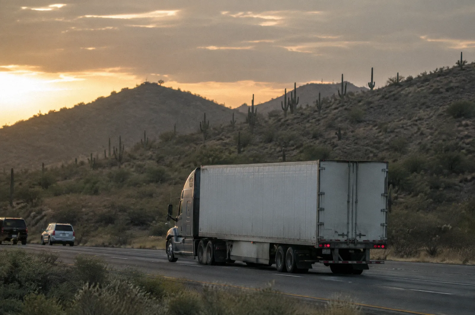 An 18-wheeler crossing a desert interstate at golden hour, long telephoto, saguaros on the hills