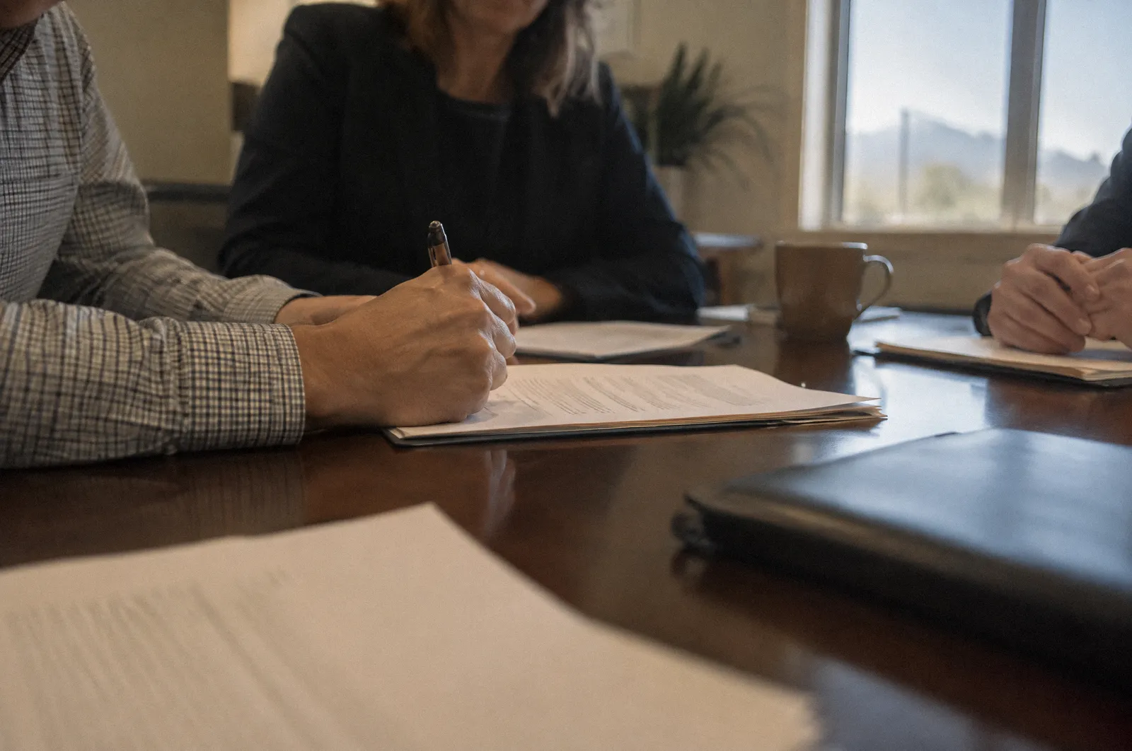 Hands signing a document at a conference table, the text unreadable, warm office light
