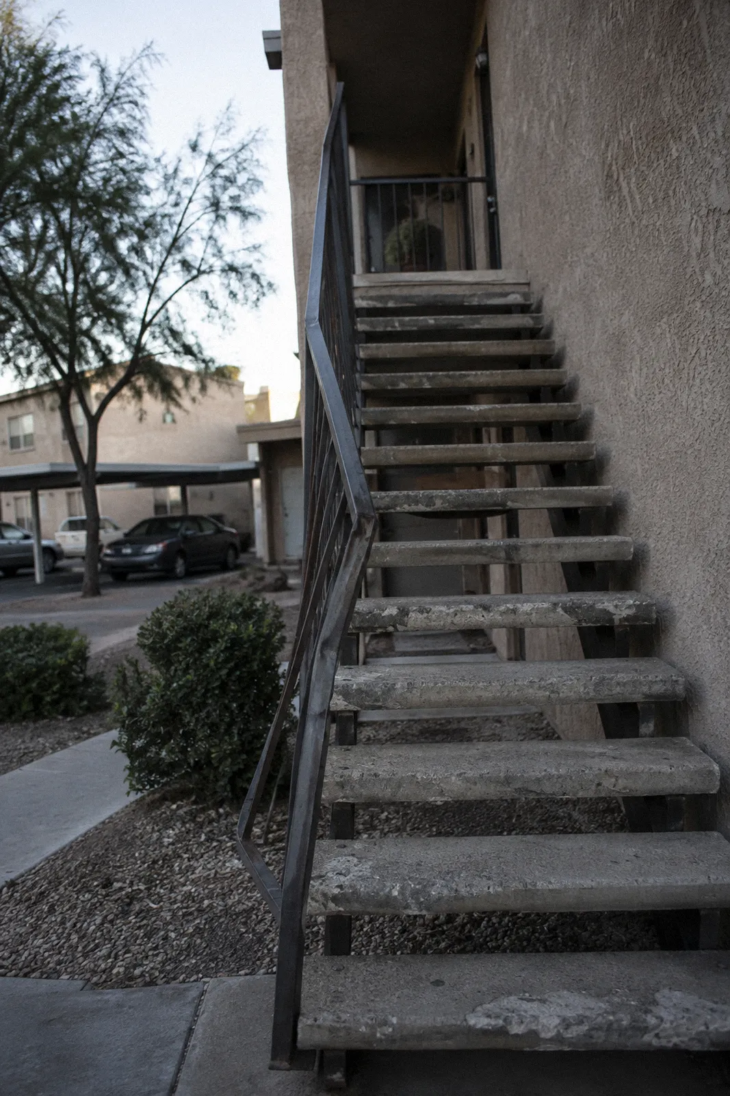 An exterior apartment staircase with a loose, bent metal handrail and worn concrete steps
