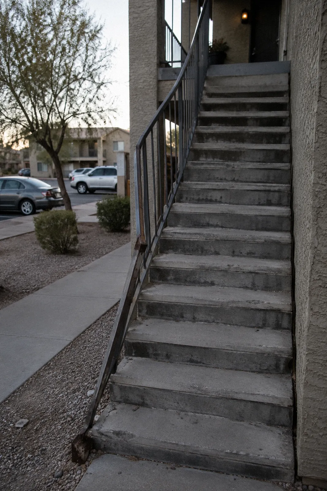 An exterior apartment staircase with a loose, bent metal handrail and worn concrete steps