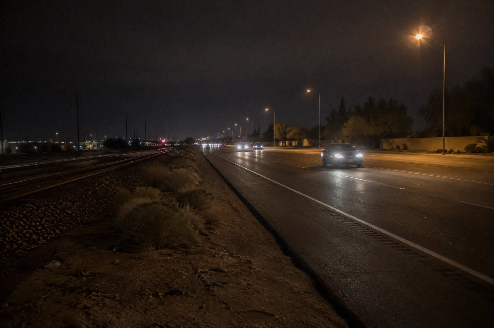 A long diagonal highway through the far West Valley near Surprise with rail tracks alongside, flat light