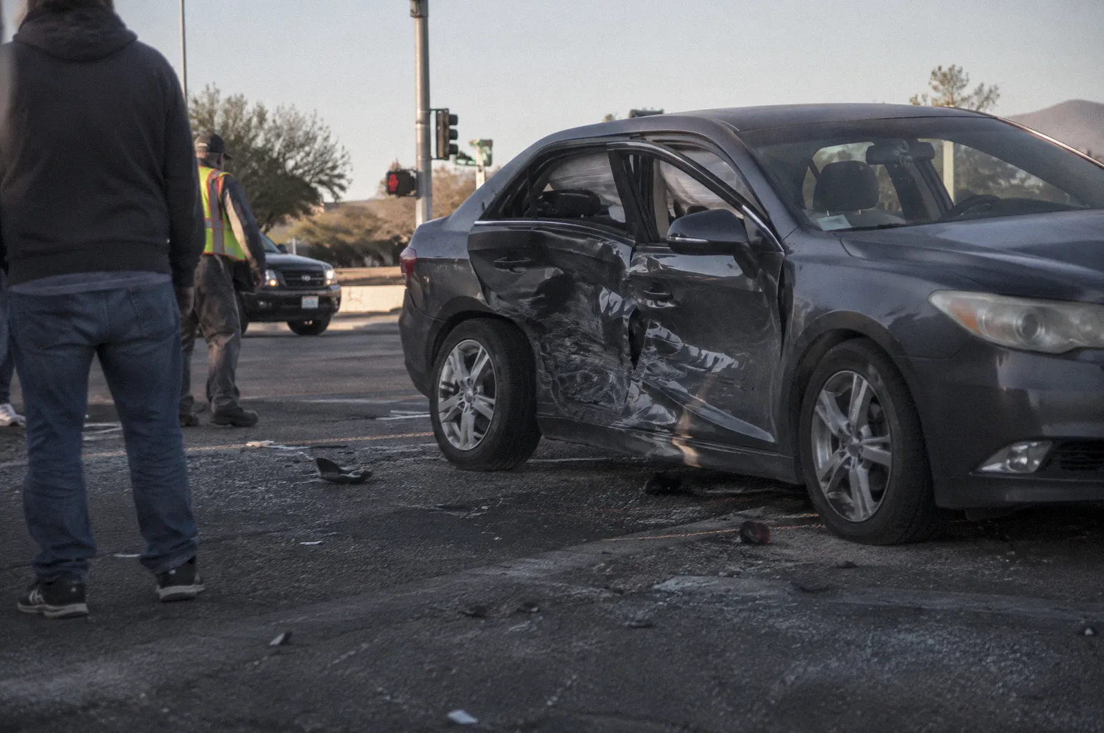 The side of a sedan caved in at the doors after a side-impact crash, stopped in an intersection, glass on asphalt