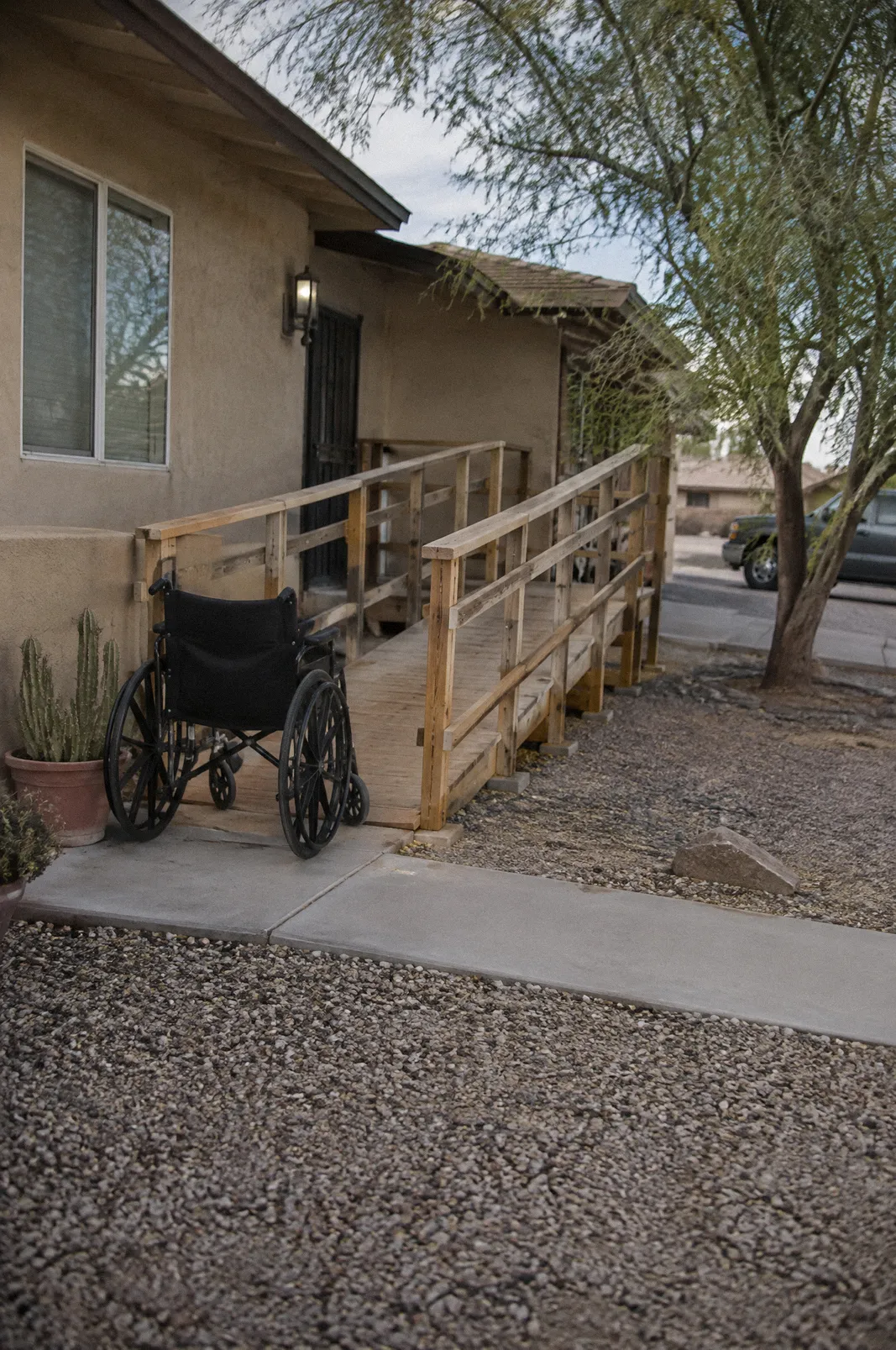 An empty wheelchair at the bottom of a new wooden ramp built onto a stucco house