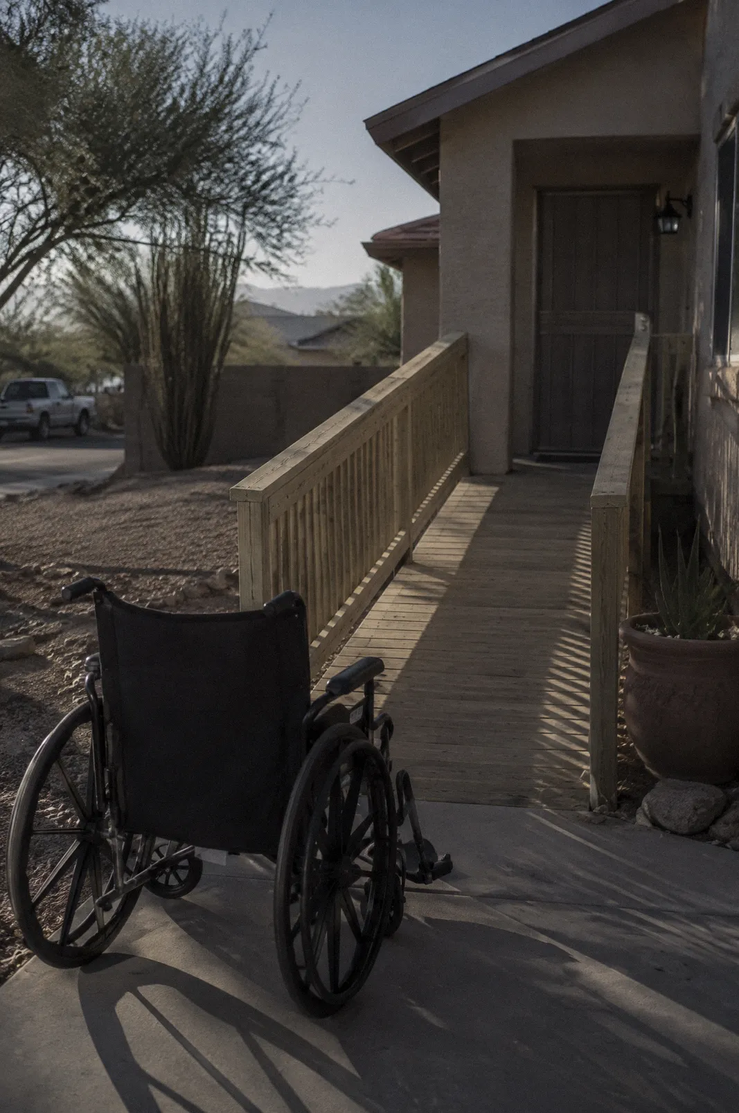 An empty wheelchair at the bottom of a new wooden ramp built onto a stucco house