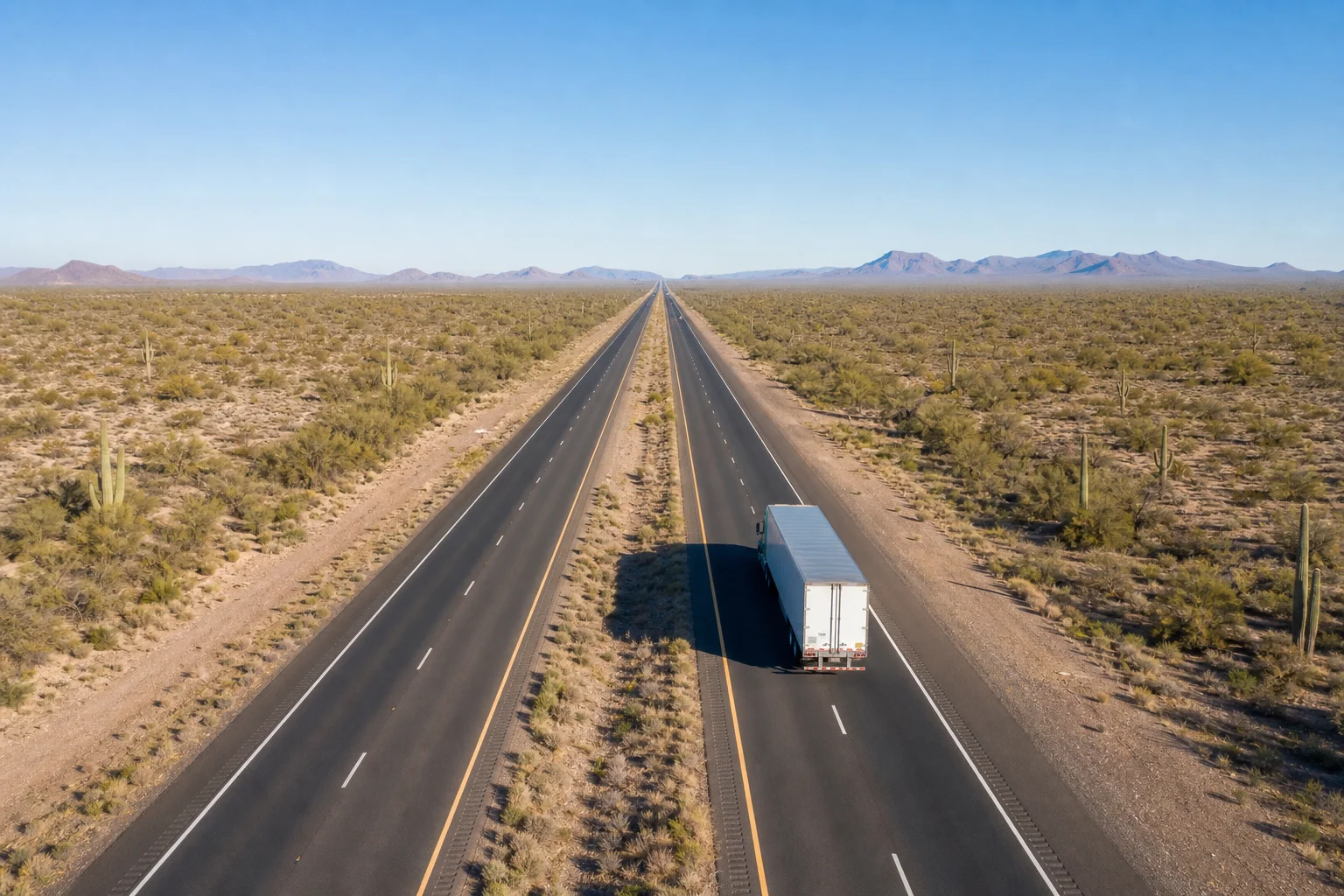 Valley Accident Law | Commercial Truck Accidents on Arizona Interstates Aerial view of a commercial semi-truck traveling on a wide Arizona interstate highway through open Sonoran Desert terrain, clear blue sky, editorial photography, no text or watermarks